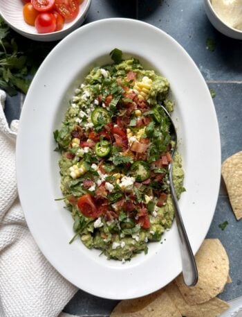 summer produce loaded guacamole in white bowl with silver spoon