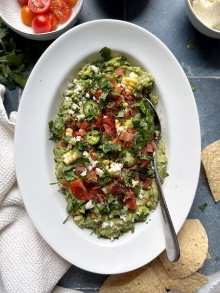 summer produce loaded guacamole in white bowl with silver spoon