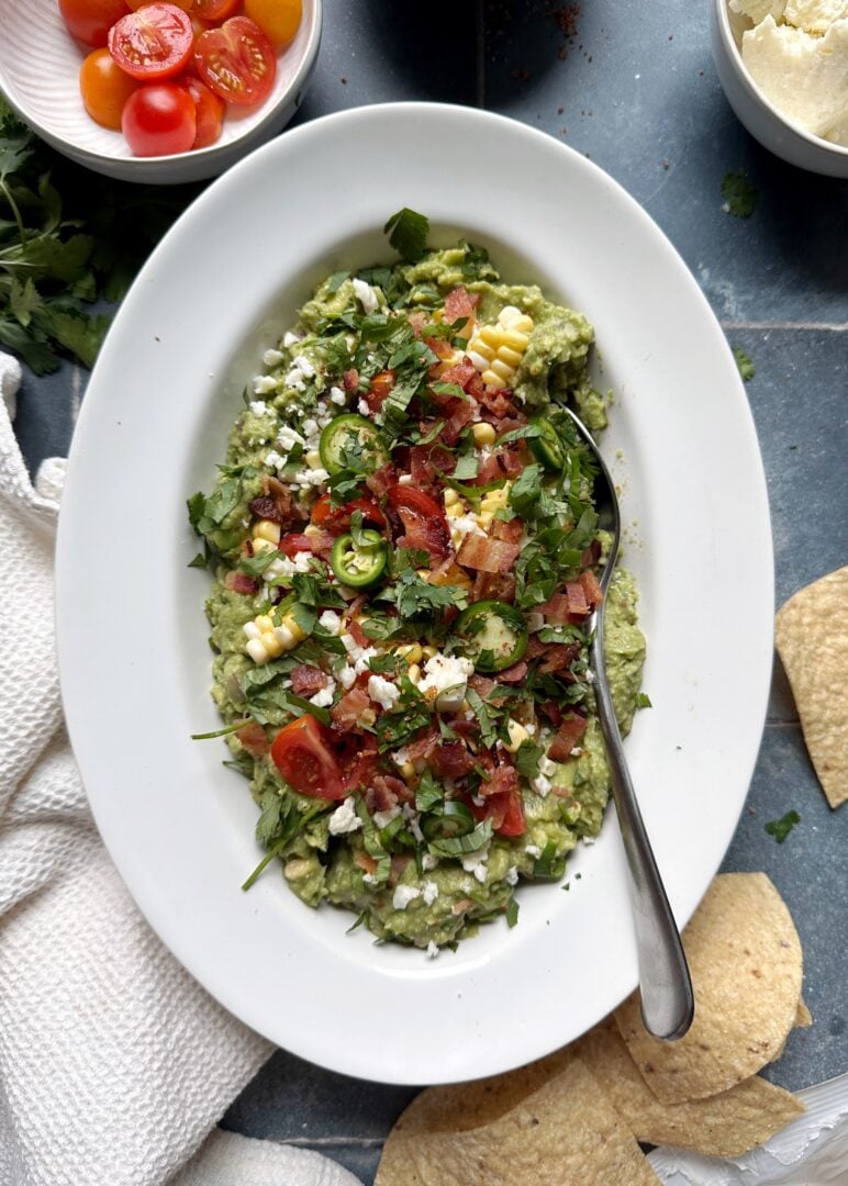 summer produce loaded guacamole in white bowl with silver spoon