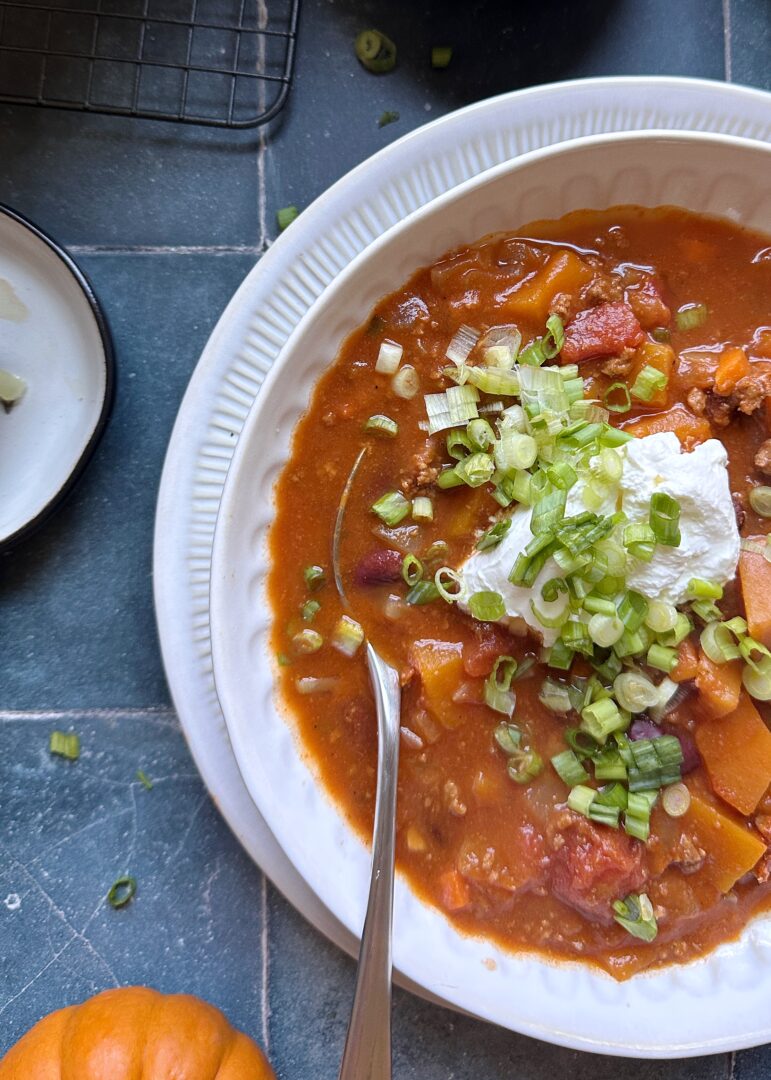 bowl of autumn harvest chili with sour cream and green onion garnish