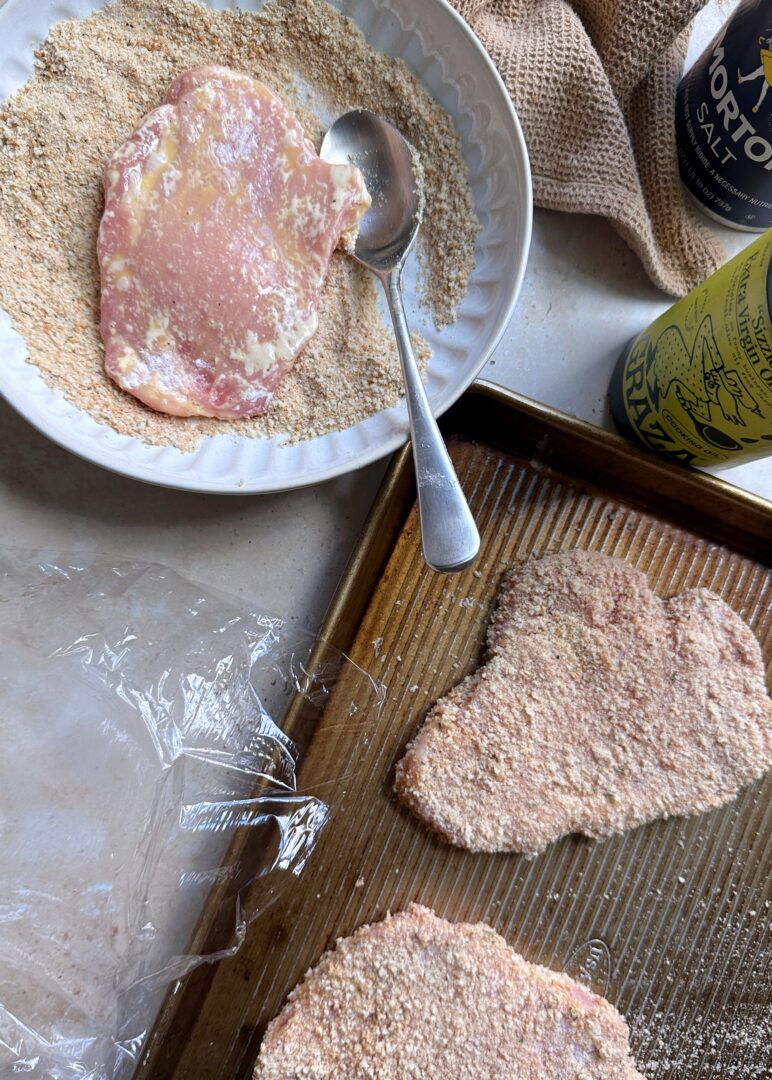 breading pork chops for schnitzel on a baking sheet
