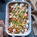 casserole dish of buffalo chicken enchiladas with ranch dressing drizzle and green onions