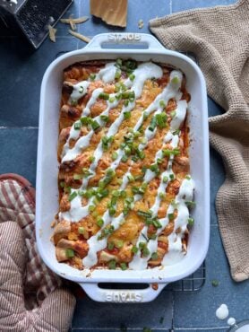 casserole dish of buffalo chicken enchiladas with ranch dressing drizzle and green onions