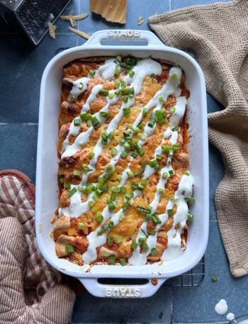 casserole dish of buffalo chicken enchiladas with ranch dressing drizzle and green onions