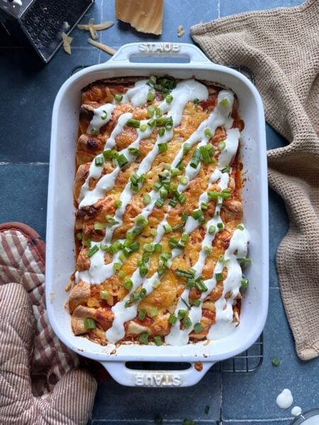 casserole dish of buffalo chicken enchiladas with ranch dressing drizzle and green onions