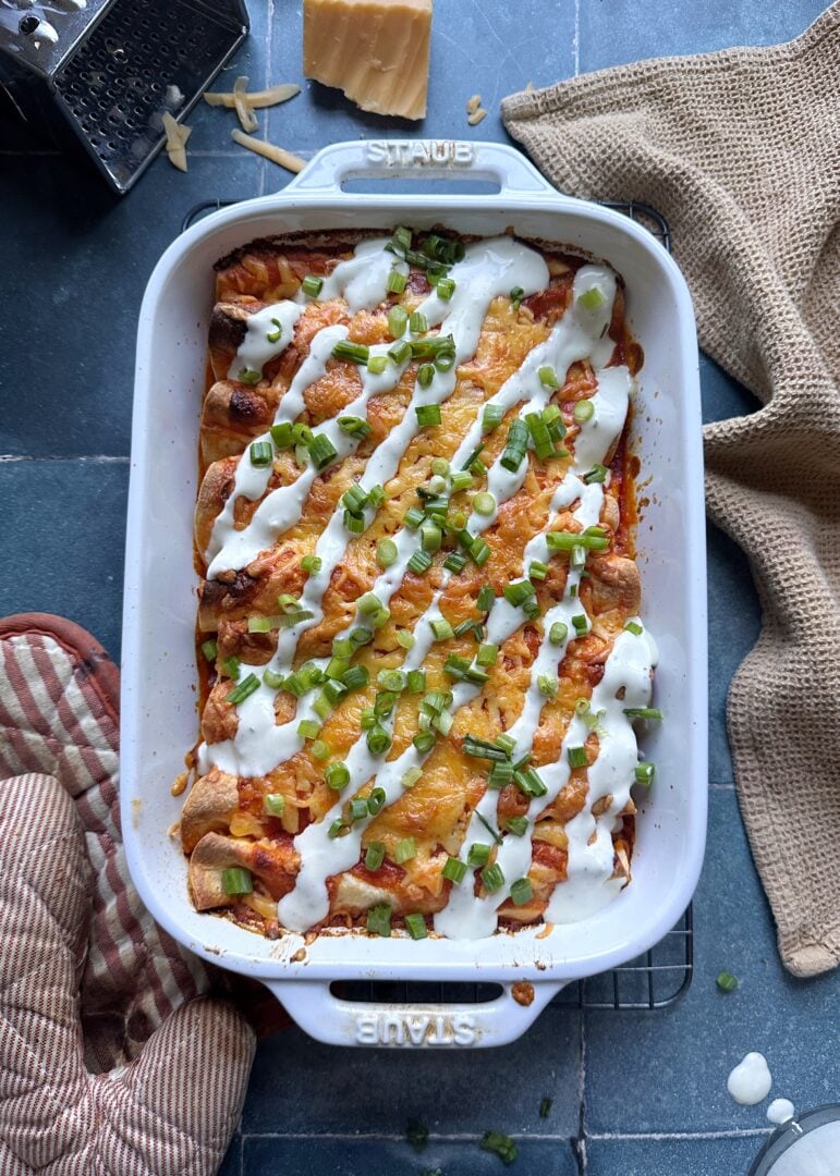 casserole dish of buffalo chicken enchiladas with ranch dressing drizzle and green onions
