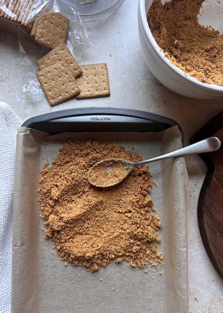 graham cracker crust poured into baking pan with spoon