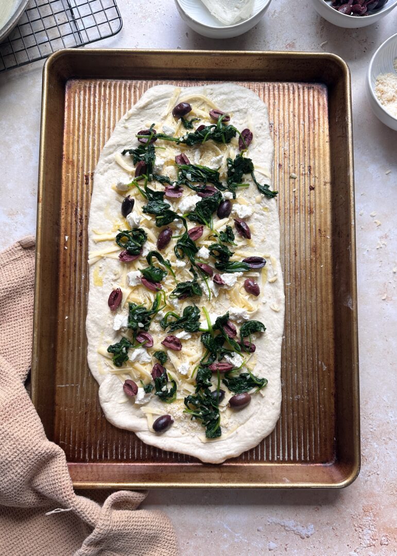 pizza crust with spinach kalamata and cheese on a pizza crust