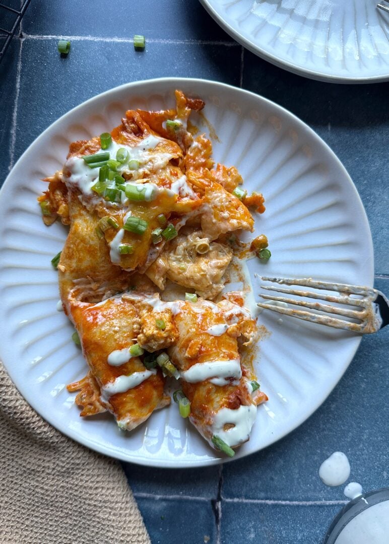 plate of buffalo chicken enchiladas with ranch dressing and green onion cut into with a fork