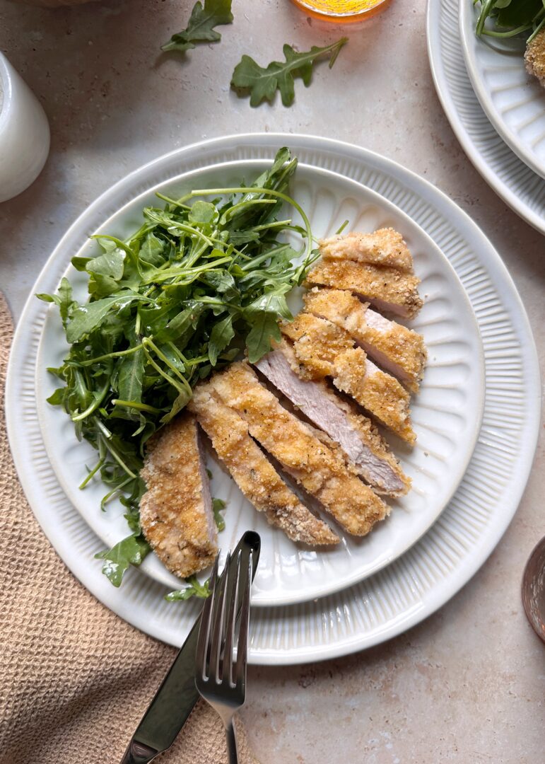 plate with sliced baked pork schnitzel and arugula salad