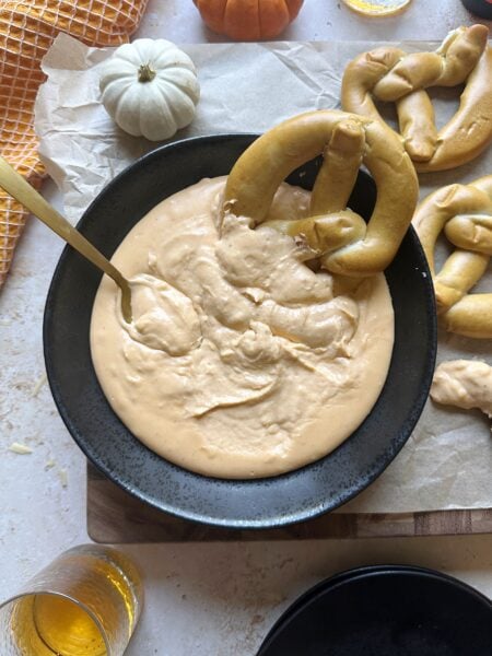 soft pretzel dipped into bowl of pumpkin beer cheese