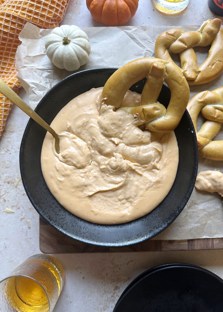 soft pretzel dipped into bowl of pumpkin beer cheese