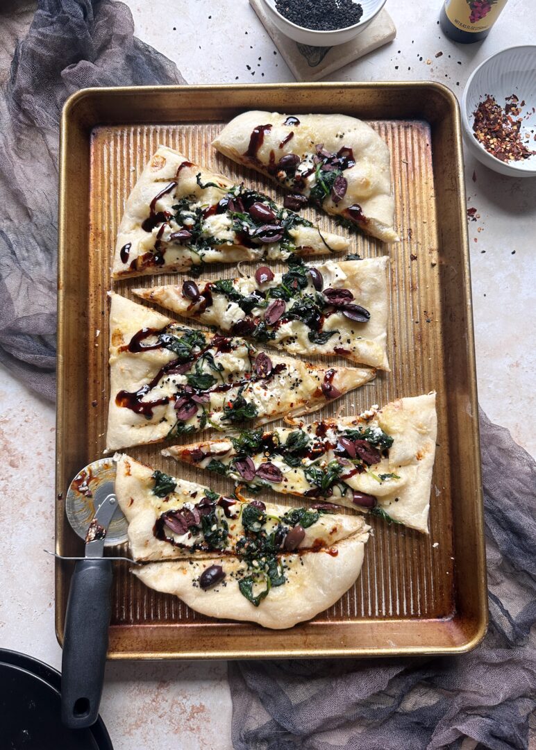 spinach kalamata and black garlic pizza sliced on a baking sheet