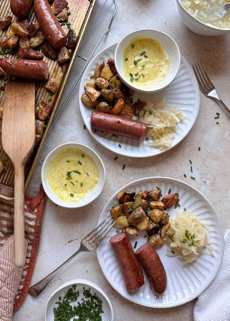 two plates of sheet pan kielbasa and potatoes with honey mustard on the side