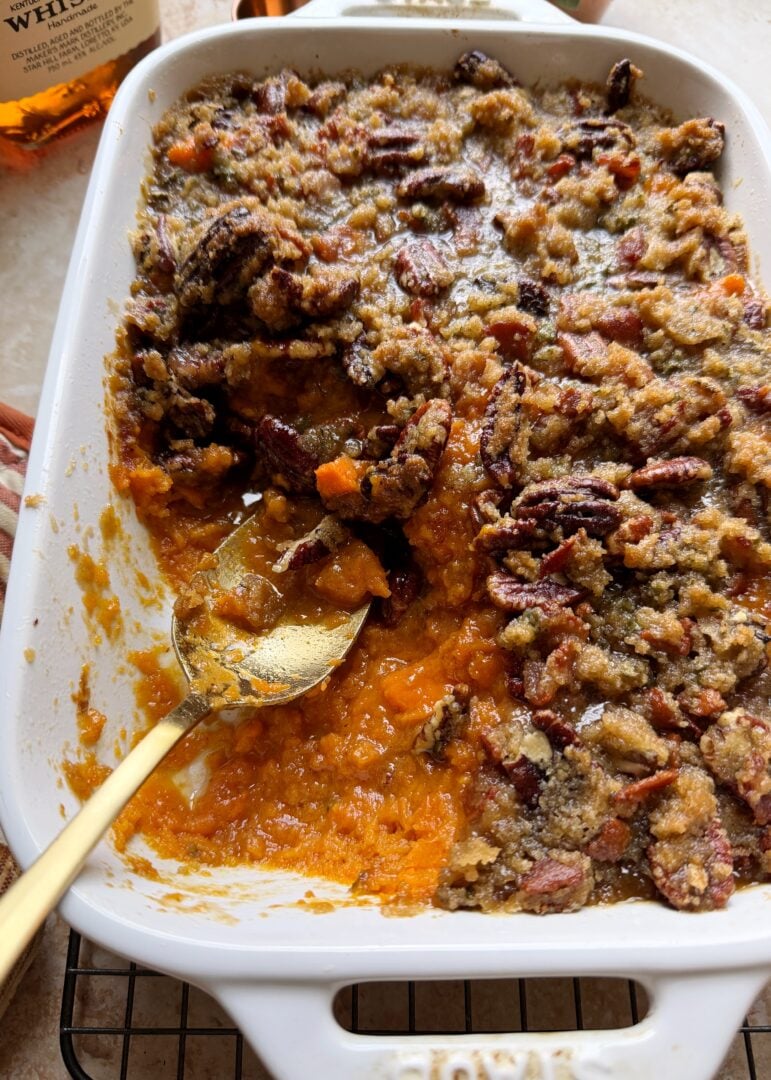 casserole dish of sweet potato casserole with bourbon and brown sugar pecan bacon topping with silver serving spoon
