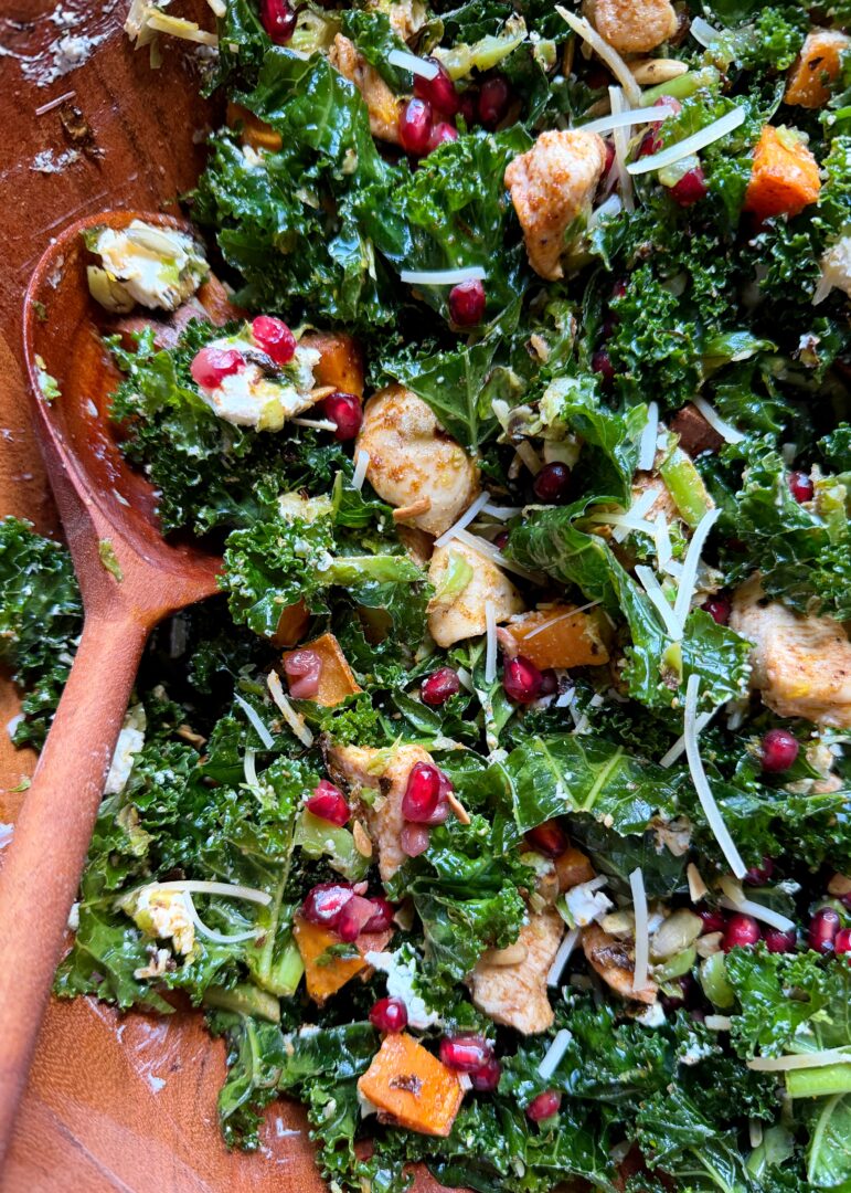 close up of roasted chicken sprouts sweet potato and kale salad in wooden bowl
