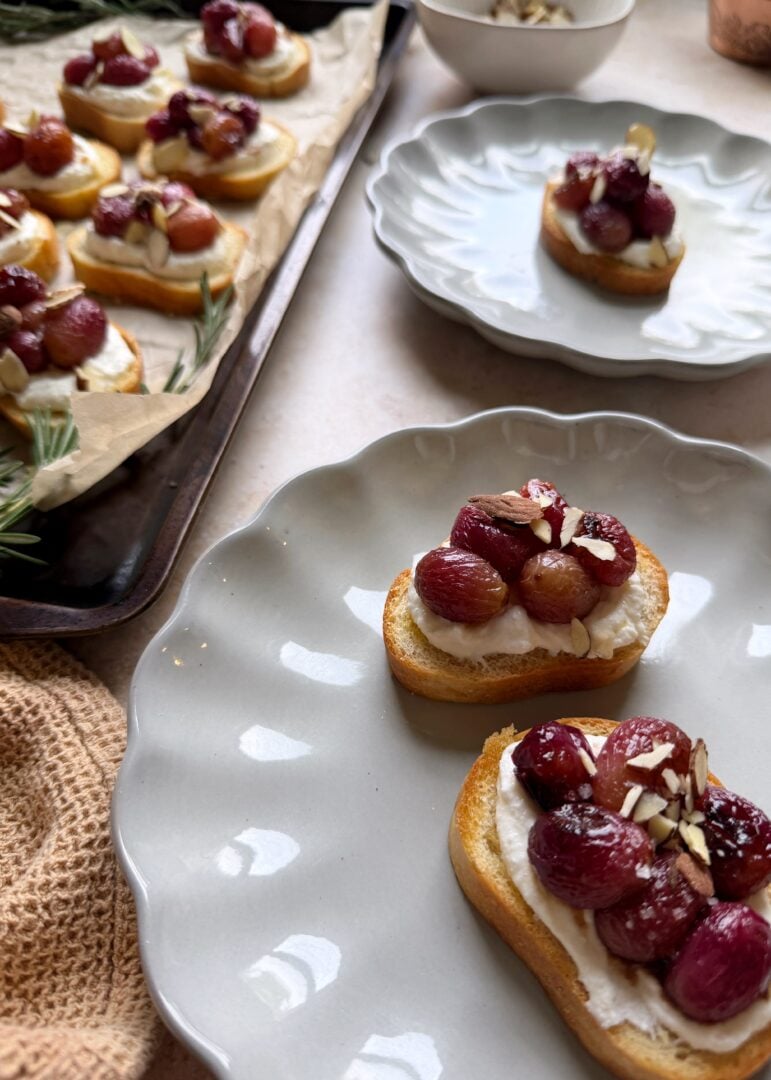 serving of roasted grape crostini with ricotta with baking sheet of more crostinis