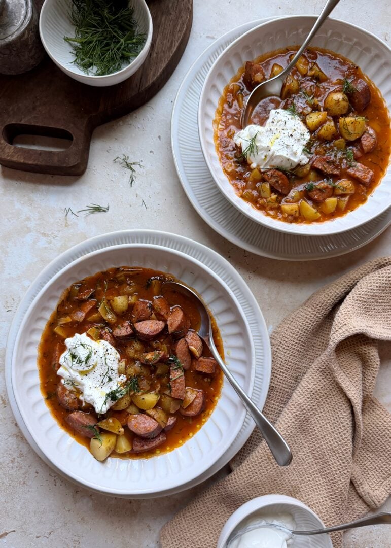 two bowls of kielbasa potato soup with sour cream and dill