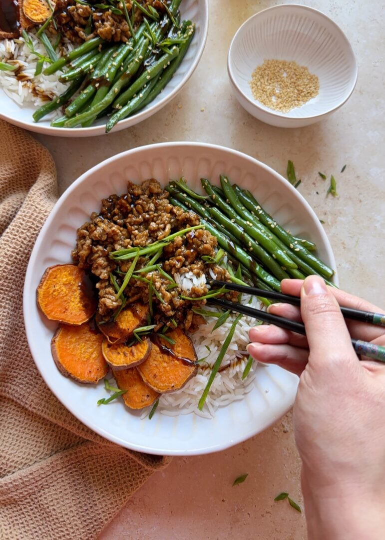 using chopsticks to get a bite of hoisin chicken stir fry with sesame green beans and roasted sweet potatoes