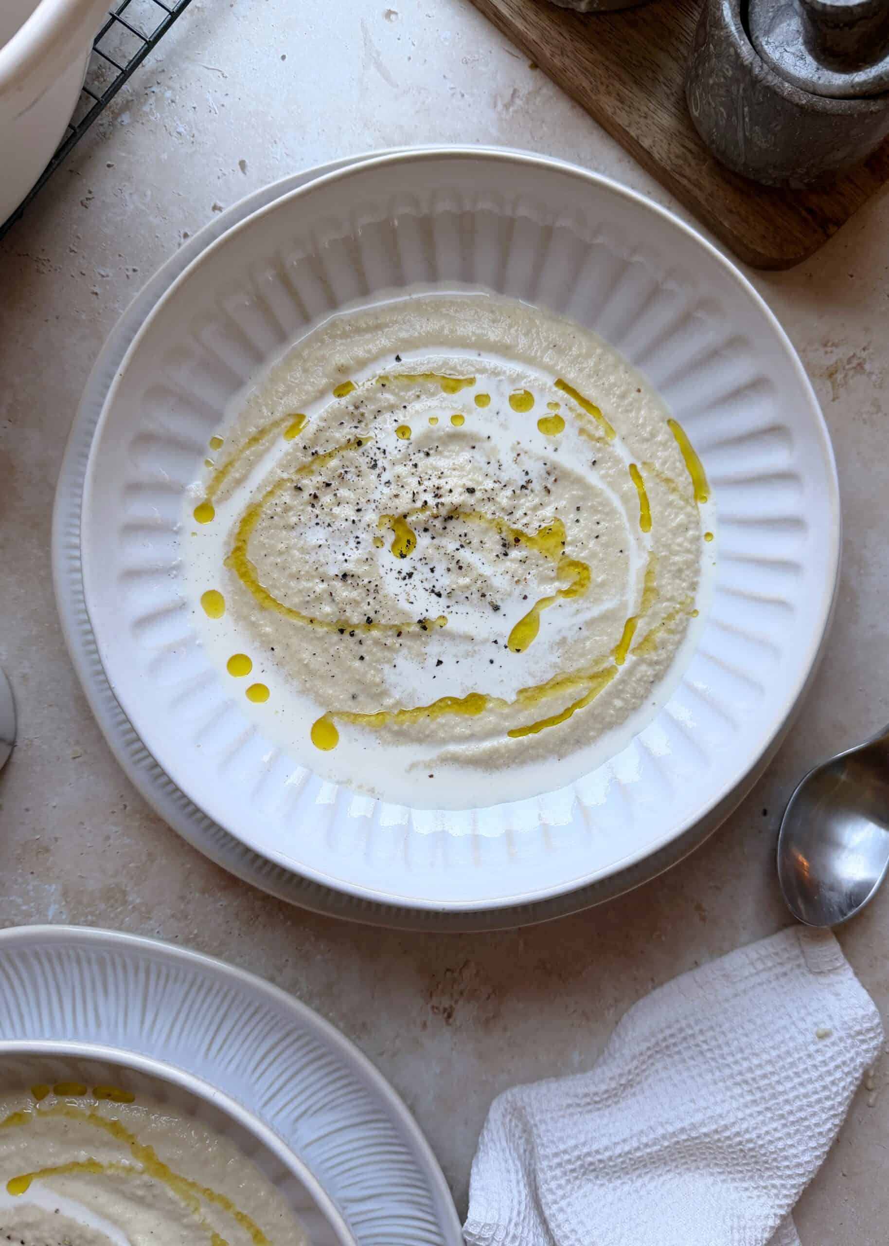 roasted cauliflower soup in a white bowl with olive oil drizzle