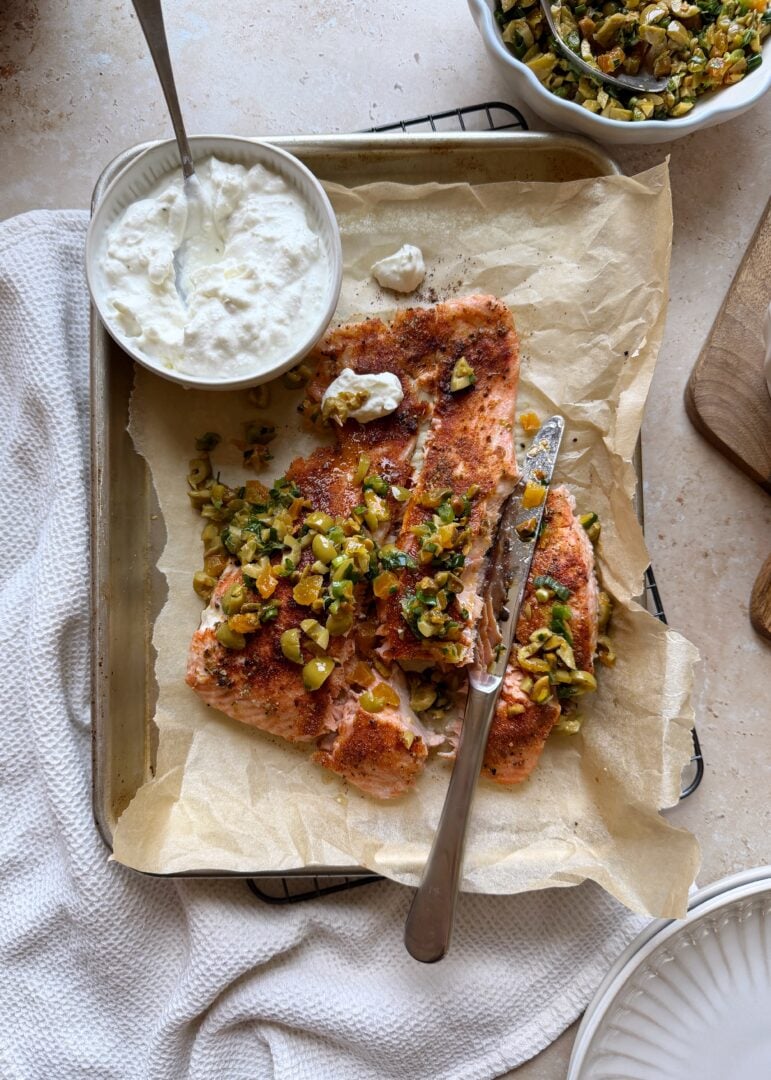 roasted salmon with olive and apricot salad on a baking sheet with feta yogurt sauce on the side