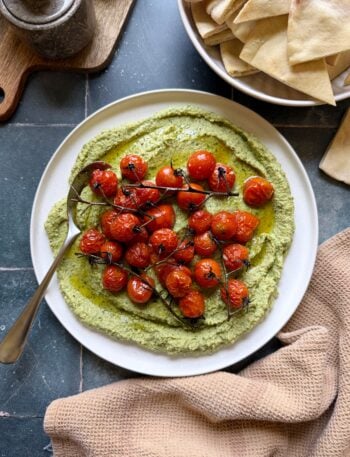 plate of herby jalapeno hummus with roasted cherry tomatoes with a serving spoon