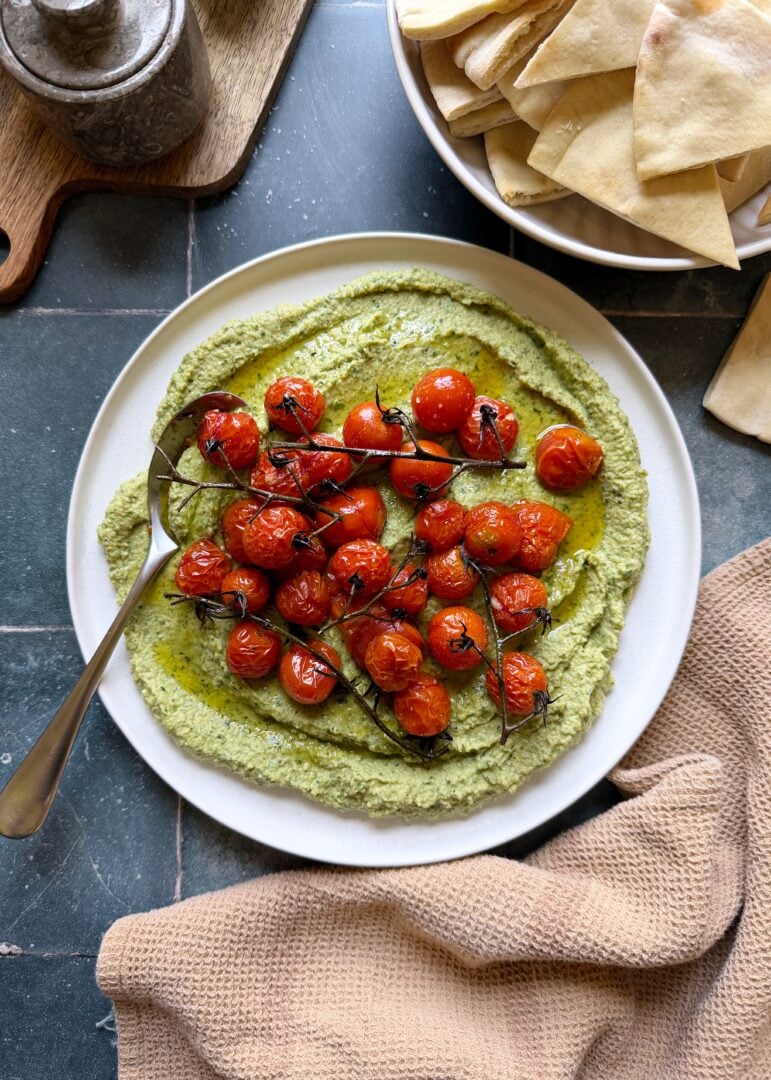 plate of herby jalapeno hummus with roasted cherry tomatoes with a serving spoon