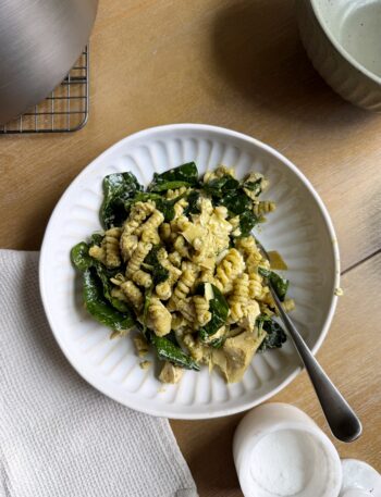 serving of creamy spinach artichoke pasta in a white pasta bowl
