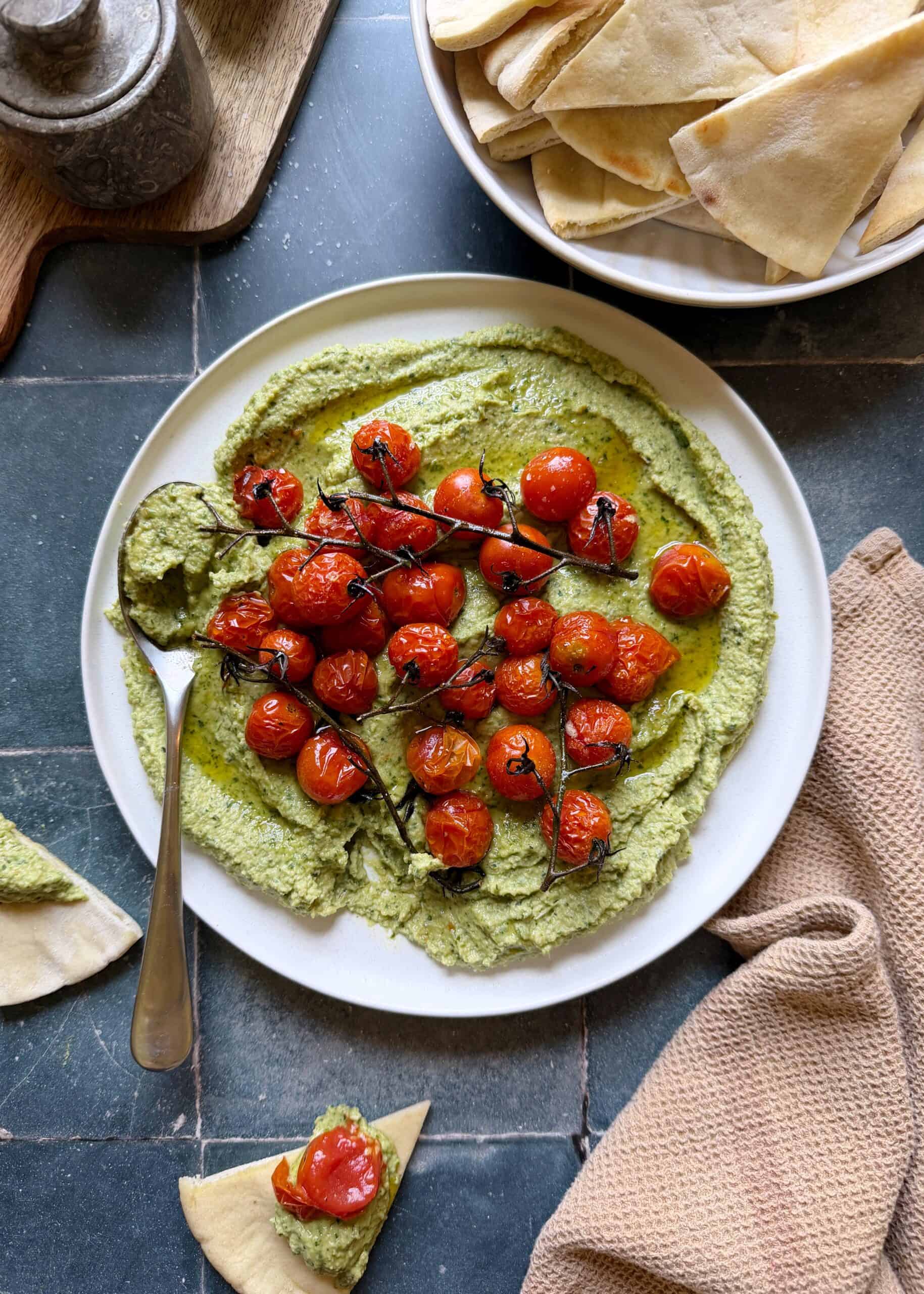serving plate of herby jalapeno hummus with roasted cherry tomatoes and pita on the side