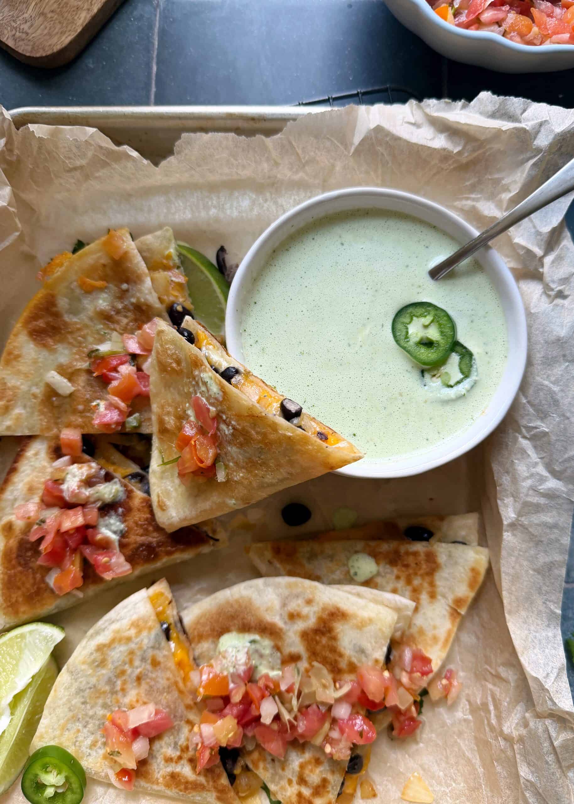 cheesy black bean quesadilla with a bite taken out of it and jalapeno cilantro sauce on the side
